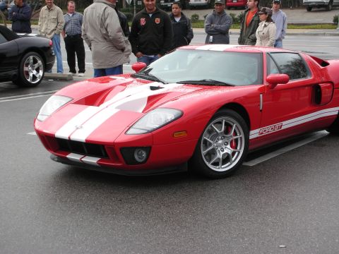 1998 Ford Crown Victoria - Red Ford GT with white racing stripes shown front three-quarter, surrounded by onlookers at a car meet.