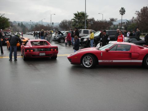 1998 Ford Crown Victoria - red Ford GT parked next to a red Ferrari Testarossa among crowds at an outdoor car gathering on a wet day.