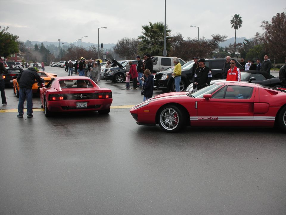 Red Ford GT beside a red Ferrari Testarossa at a crowded outdoor car meet