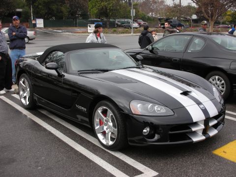1998 Ford Crown Victoria - Black Dodge Viper convertible with twin silver stripes, parked front three-quarter on a marked lot with onlookers.