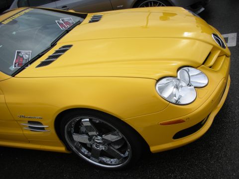 1998 Ford Crown Victoria - Front fender of a yellow Mercedes-Benz SL roadster with a large chrome wheel and event stickers on the windshield.
