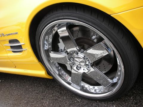 1998 Ford Crown Victoria - Detailed close-up of a polished chrome multi-spoke wheel with a cross-drilled rotor on a yellow sports car.