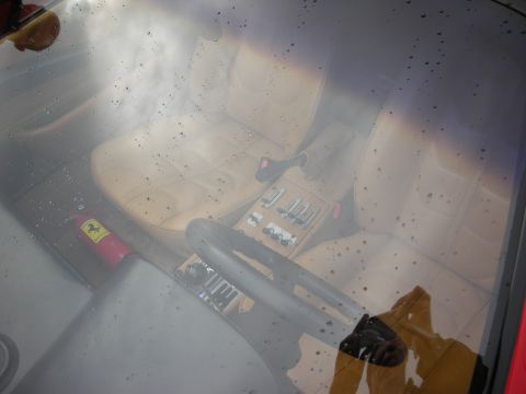 1998 Ford Crown Victoria - Tan leather interior of a Ferrari with gated shifter, viewed through a rain-spotted side window with a photographer reflected.