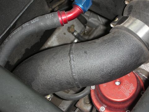 1998 Ford Crown Victoria - Detail of black wrinkle-finish intake piping with red and blue AN fittings and a red blow-off valve on a turbocharged engine.