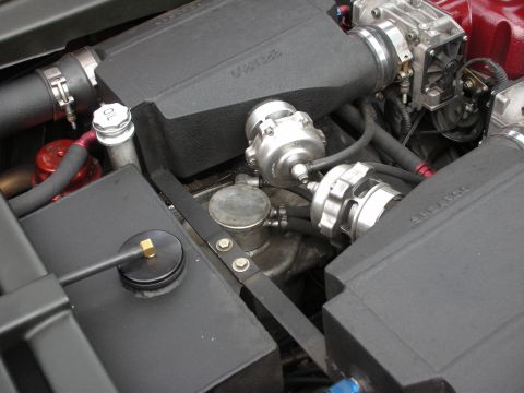 1998 Ford Crown Victoria - Close-up inside an engine bay showing a turbocharger, wastegate, and braided hoses surrounded by black covers.