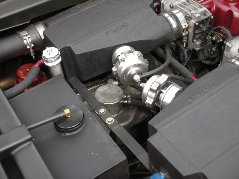 Engine-bay close-up of a turbocharger and wastegate amid black covers and hoses