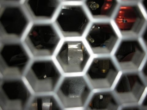 1998 Ford Crown Victoria - View through a silver honeycomb mesh of an engine bay showing black and red components and a blue anodized fitting.