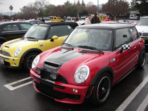 1998 Ford Crown Victoria - red Mini Cooper S with black hood stripe and checkered mirror sits beside a yellow Mini convertible in a parking lot.