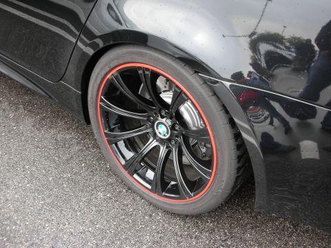 1998 Ford Crown Victoria - Close-up of a glossy black multi-spoke BMW wheel with a red rim pinstripe and BMW roundel center cap on a black car.