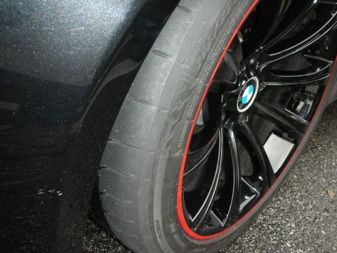 1998 Ford Crown Victoria - Close-up of a black multi-spoke BMW wheel with red rim pinstripe and low-profile tire on a dark metallic car.