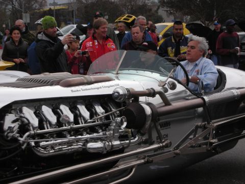 1998 Ford Crown Victoria - white-haired man drives a polished silver hot rod with an exposed Banks-turbocharged V12, a crowd photographing it.