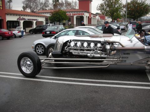 1998 Ford Crown Victoria - long polished silver hot rod with exposed Banks turbo Chrysler V12 and chrome front wheels parked outside a bank.