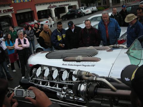 1998 Ford Crown Victoria - Spectators gather around the polished front of a hot rod displaying a chrome Banks Turbocharged Chrysler V12 engine.