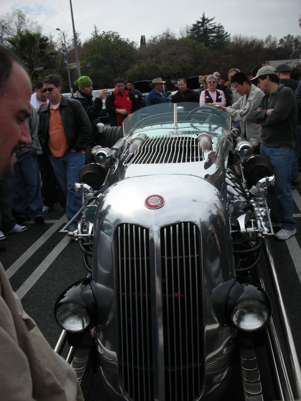 Front view of a polished silver hot rod with chrome grille and exposed engine