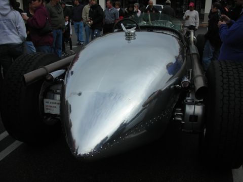 1998 Ford Crown Victoria - Rear of a polished silver teardrop-bodied streamliner hot rod with dual rear tires and a small round taillight, crowd behind.