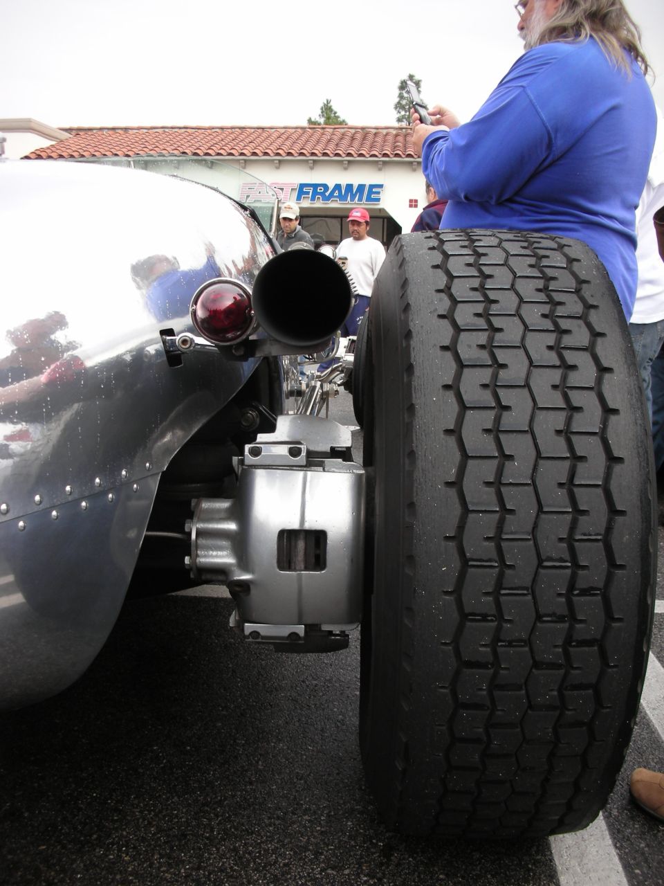 Rear of a silver hot rod with large exhaust outlet beside a dual rear wheel
