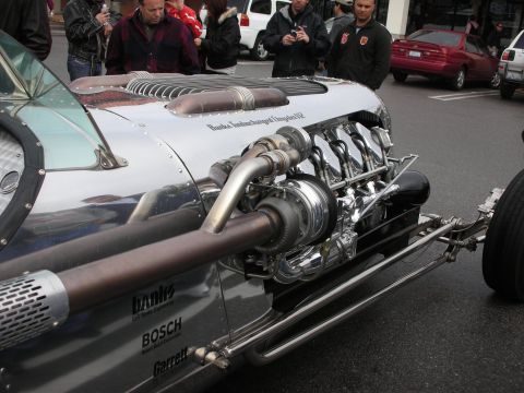 1998 Ford Crown Victoria - Side view of a long polished silver hot rod with an exposed Banks-turbocharged V12, large turbo, and chrome side pipe.