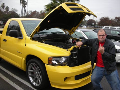 1998 Ford Crown Victoria - man gives a thumbs-up beside a yellow Dodge Ram SRT-10 pickup with its hood scoop raised.