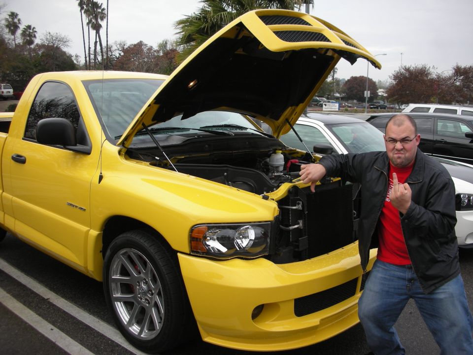 Man poses by a yellow Dodge Ram SRT-10 pickup with hood open