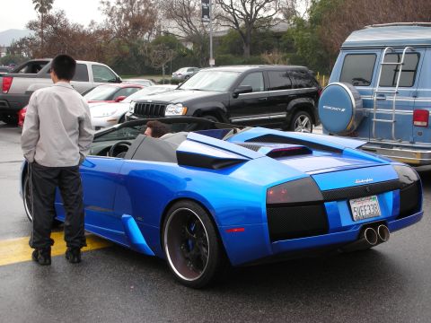 1998 Ford Crown Victoria - blue Lamborghini Murcielago roadster seen from the rear, a man peering into its open cockpit.