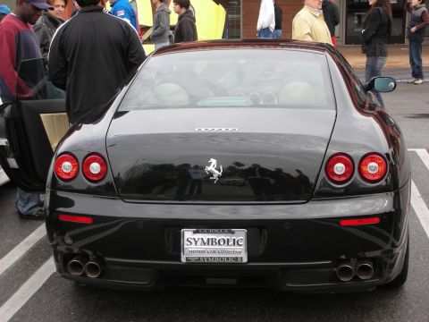 1998 Ford Crown Victoria - black Ferrari coupe viewed from the rear with quad exhaust and a SYMBOLIC dealer license plate.