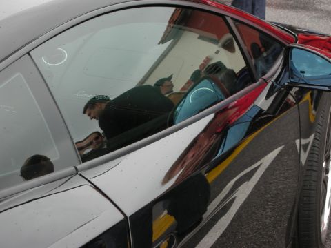 1998 Ford Crown Victoria - side glass and rear quarter of a black Lamborghini with onlookers reflected in the paint.