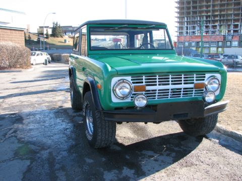 1975 Ford Bronco - Front view of a green 1975 Ford Bronco parked on a wet asphalt surface.