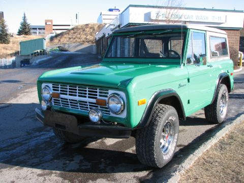 1975 Ford Bronco - A classic green 1975 Ford Bronco with a white hardtop sits parked in front of a car wash.