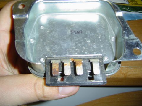 1979 Ford Bronco - A metal electrical component, possibly a voltage regulator, is held in a hand, showing four prongs and stamped text.