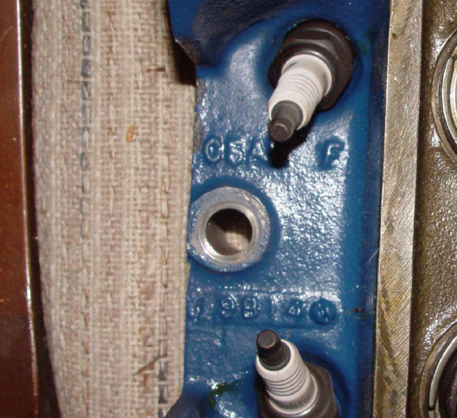 Blue engine part with "C5A F" and "199140" cast into it, and two spark plugs installed