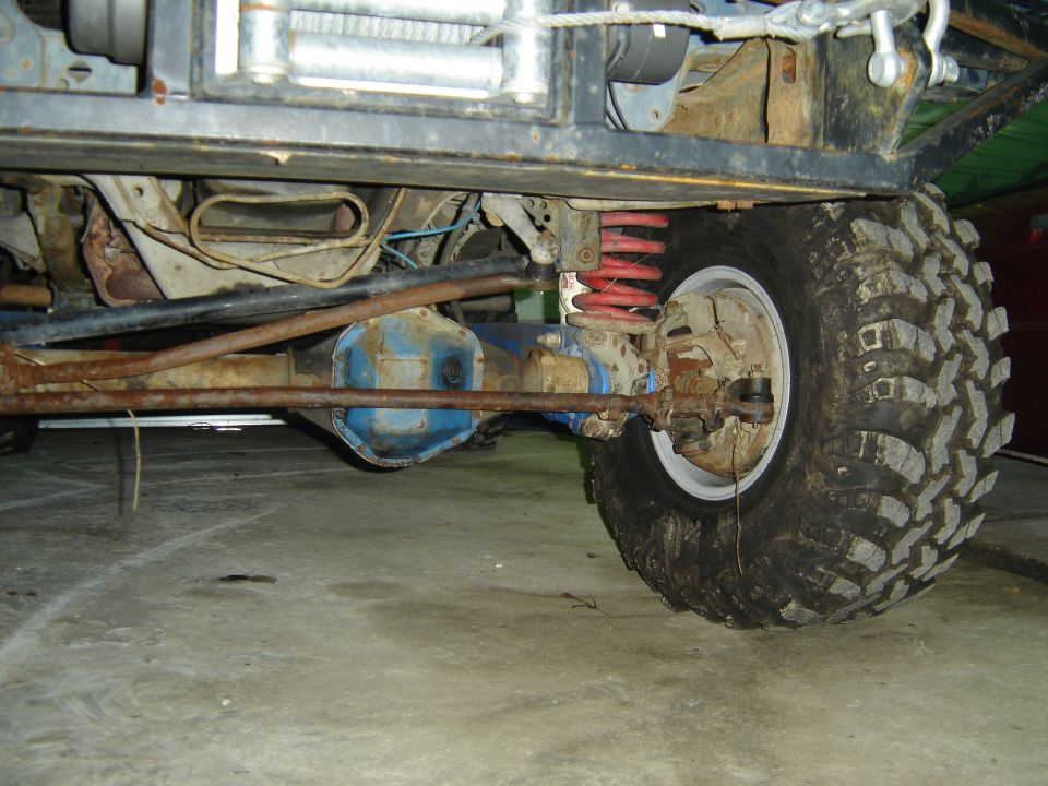 Underside of lifted Bronco showing blue diff, red coil spring, and mud tire
