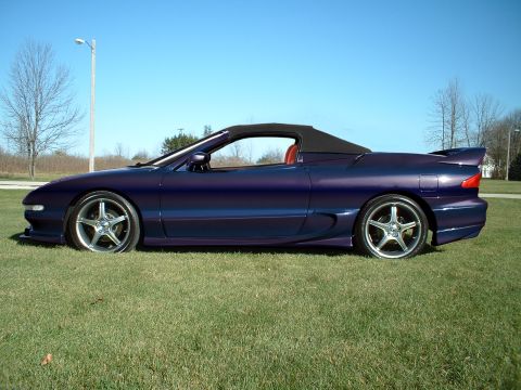 1995 Ford Probe - Side profile of a purple 1995 Ford Probe convertible parked on grass under a clear blue sky.