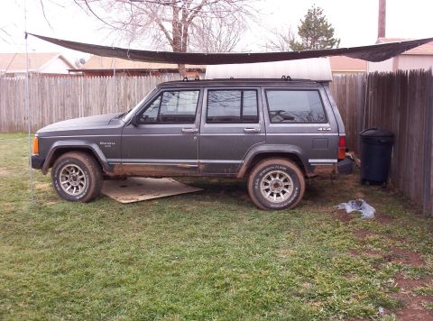 1987 Jeep Cherokee - A gray Jeep Cherokee is parked on a grassy area next to a wooden fence.