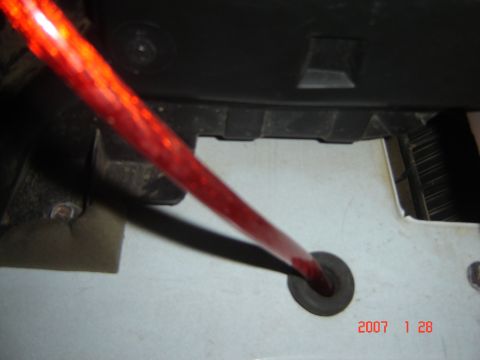 1993 Ford Bronco - A red wire is threaded through a rubber grommet in a white surface, with black plastic trim overhead.