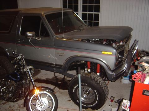 1986 Ford Bronco - A gray Ford Bronco with its hood open and lifted suspension is parked indoors next to a motorcycle.