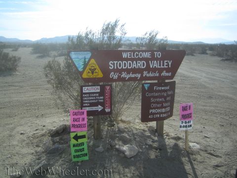 1990 Ford Bronco - brown 'Welcome to Stoddard Valley Off-Highway Vehicle Area' sign with pink race-in-progress and caution placards.