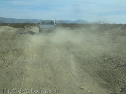 1990 Ford Bronco - white truck raises a cloud of dust as it drives over a rough, washed-out desert dirt road.