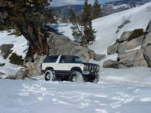 1986 Ford Bronco - A white and blue Ford Bronco navigates a snowy mountain path.