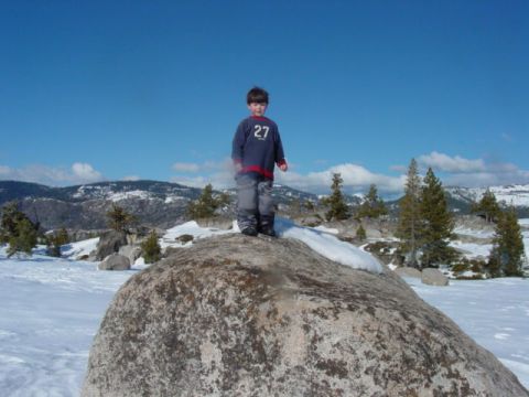 1986 Ford Bronco - A young boy stands atop a large boulder in a snow-covered landscape with mountains in the background.