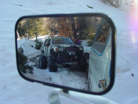 1986 Ford Bronco - A heavily modified pickup truck navigates a snowy trail, seen through the reflection of a side mirror.