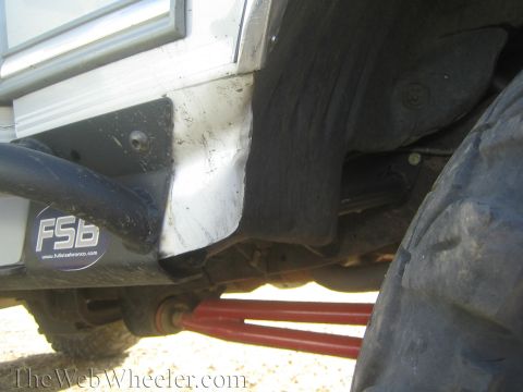 1990 Ford Bronco - Underside of a lifted white off-road truck showing the red track bar, sway bar, and a Full Size Bronco mud flap.
