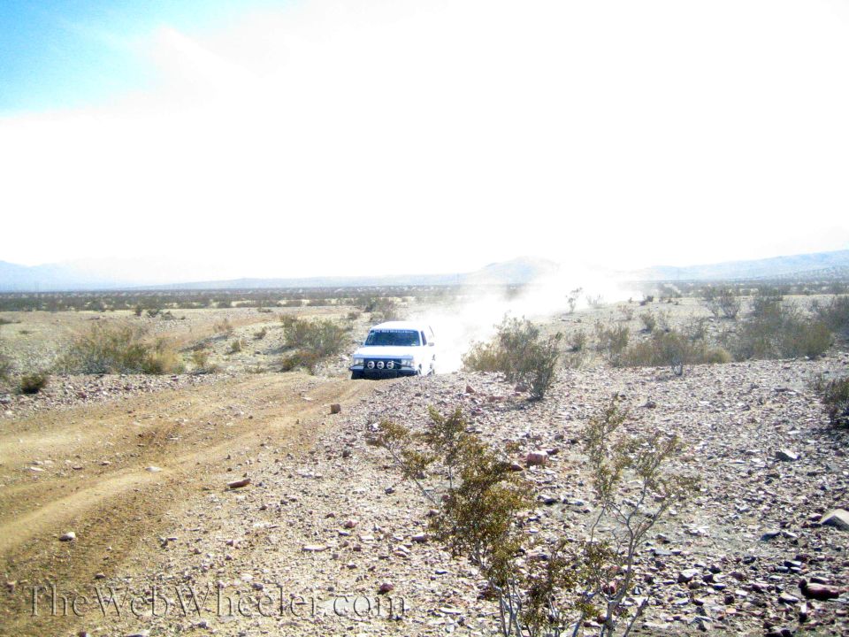 White off-road vehicle with light bar driving a dusty rocky desert track