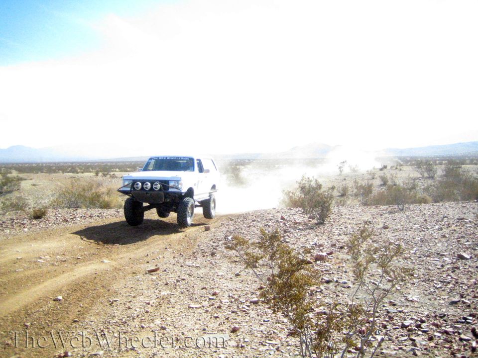 White lifted SUV with off-road lights cresting a dusty desert ridge