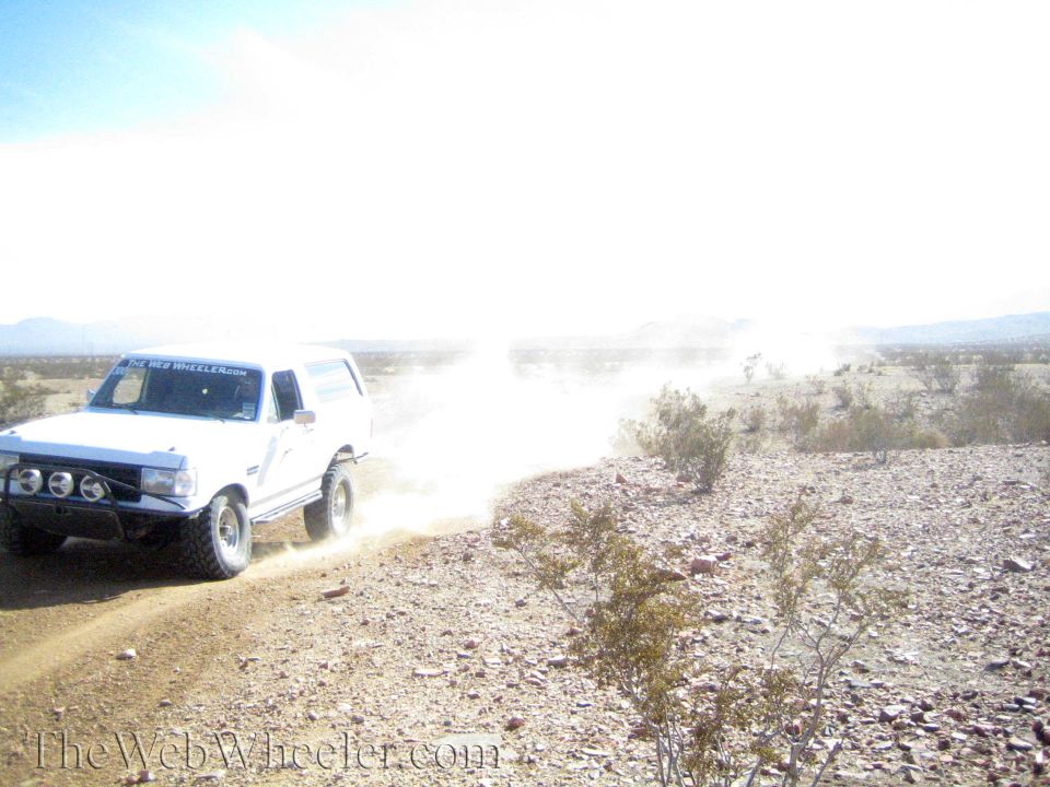 White Ford Bronco with light bar driving fast on a dusty desert trail