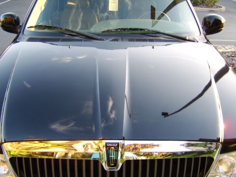 1996 Mercury Grand Marquis - Front-end view of a black Lincoln sedan photographed over the hood, showing the chrome grille and a Lincoln badge emblem in the center. The…