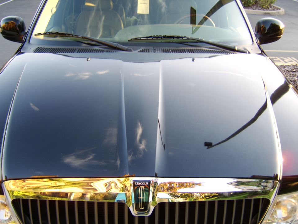 Black Lincoln sedan front hood and chrome grille with Lincoln badge, reflections visible