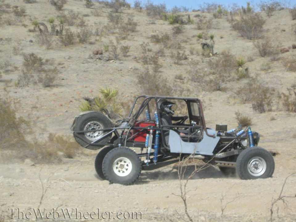 Open tube-frame off-road buggy with rear-mounted spare on a desert trail