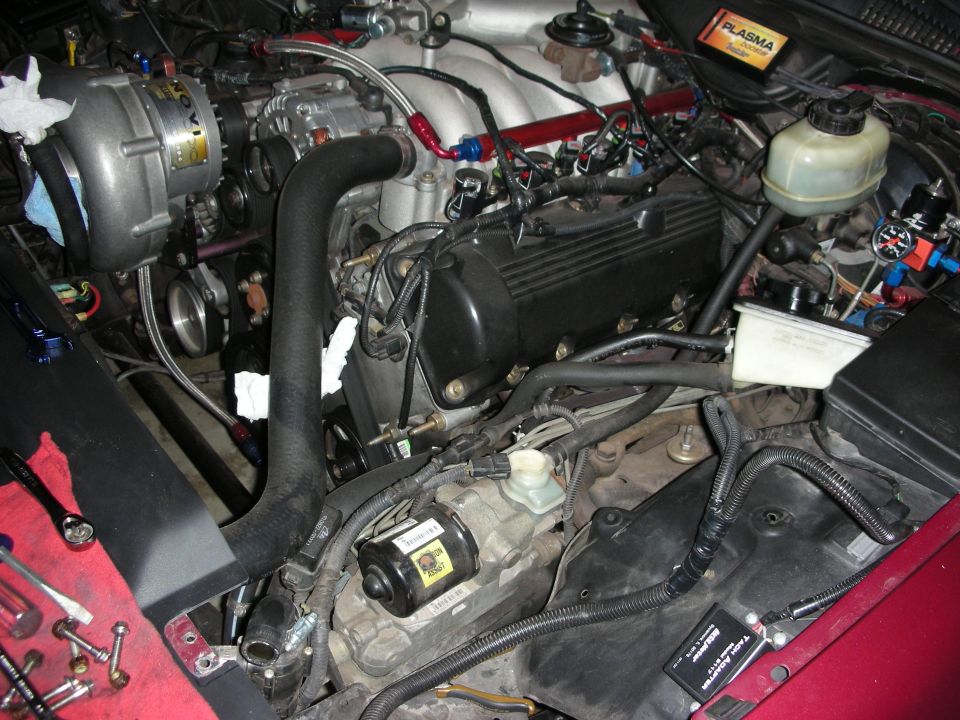 Engine bay with a silver supercharger, black engine cover, and red fender. Tools are on a red cloth