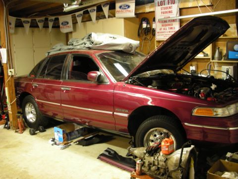 1992 Ford Crown Victoria - A maroon Ford Crown Victoria is parked in a garage, undergoing maintenance with its hood open and parts laid out.