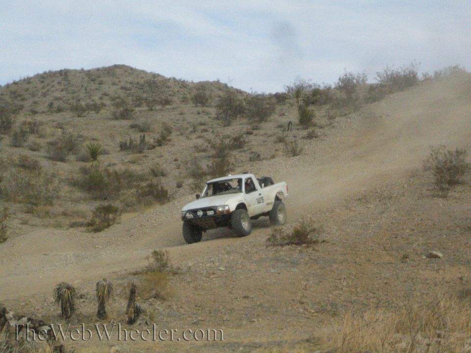 White off-road pickup truck driving up a dusty desert hillside trail